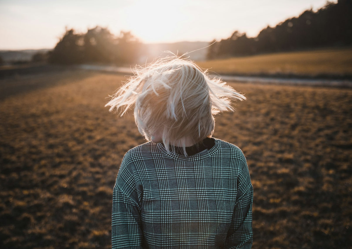 Person with short, pale blond hair moving across their face outdoors at sunset.