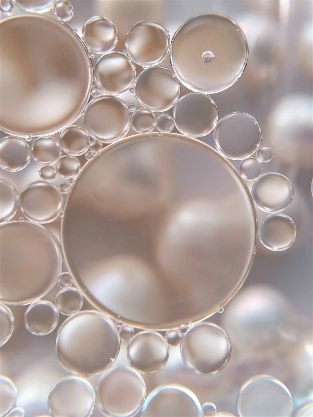 Close-up of rounded oil droplets in water with soft champagne and silver reflections.