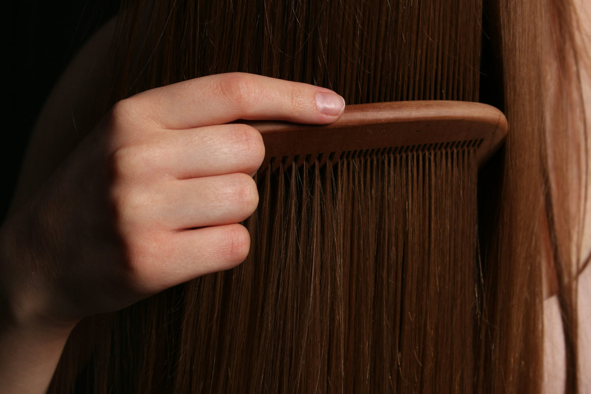 Close-up of a hand gently combing long brown hair with a wooden comb.
