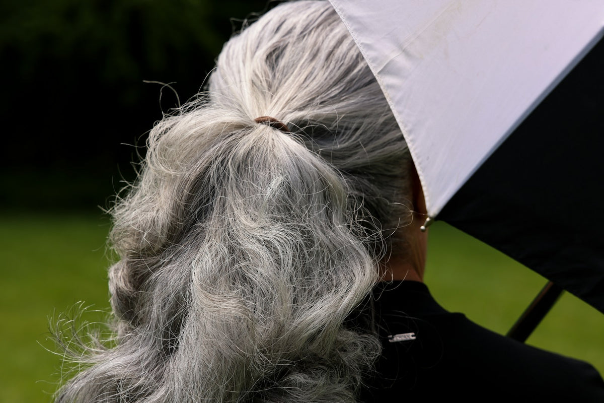 Back view of long silver-gray hair tied in a ponytail beside a black-and-white umbrella.
