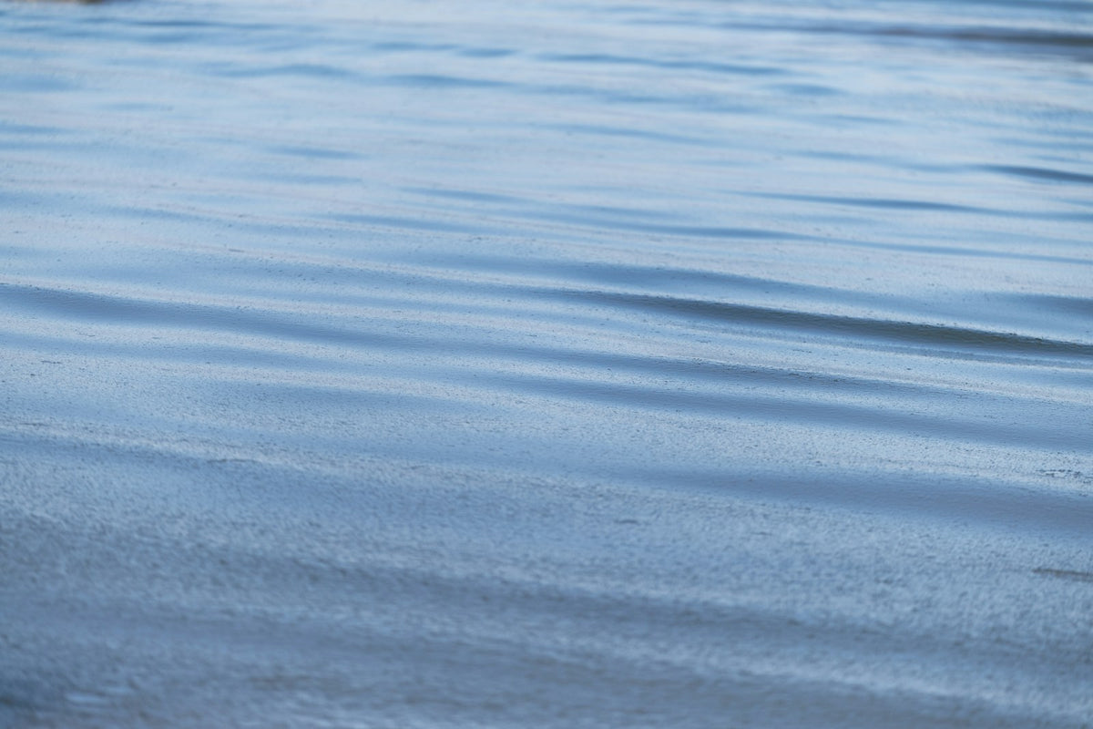 Gentle ripples and soft reflections across a pale blue water surface.